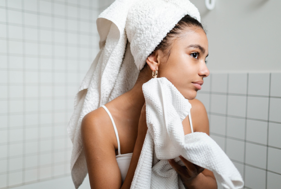 This is a photo of a woman in her bathroom after her shower wearing a towel and drying her face.